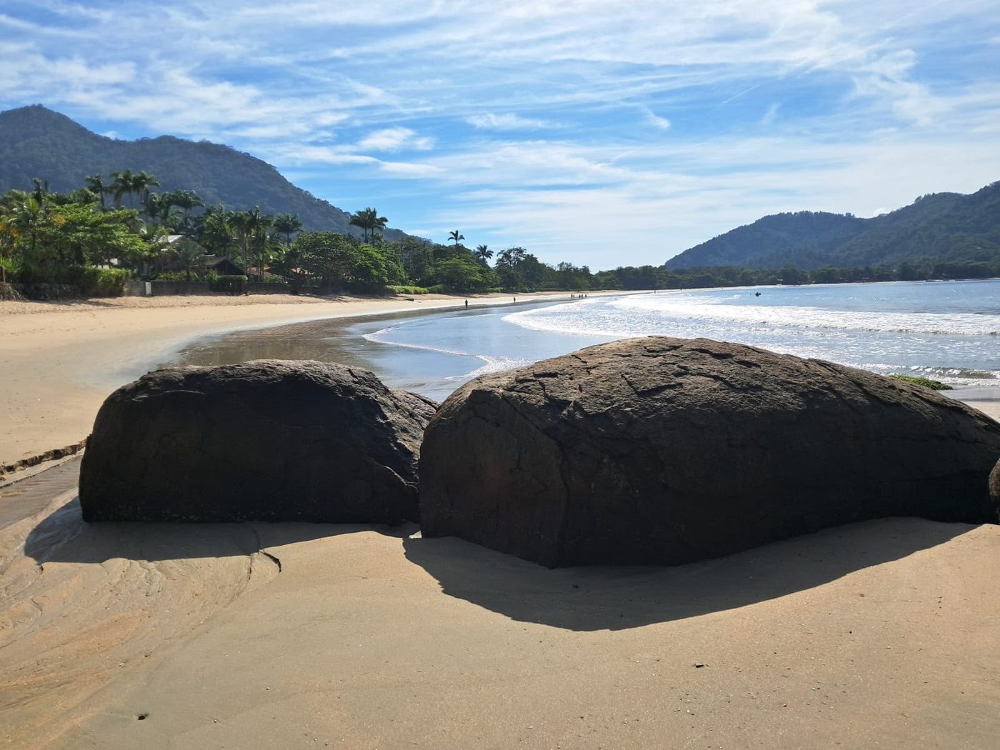 Praia Domingas Dias com pedras na areia, mata e morros ao fundo
