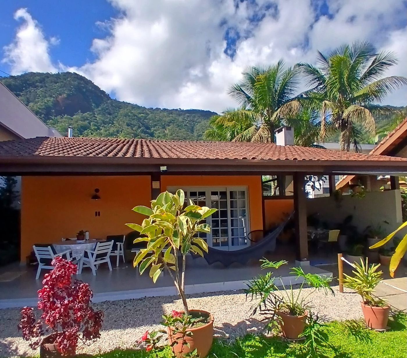 Fachada laranja da casa com varanda, rede e a Mata Atlântica ao fundo