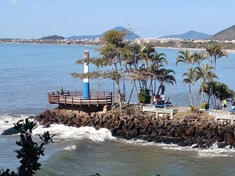 Farol azul e branco sobre as pedras, com mirante de madeira