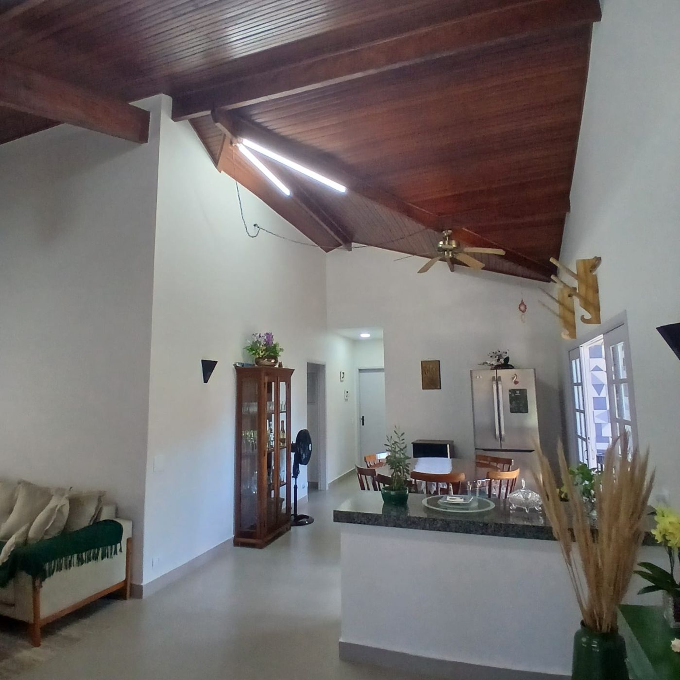 Sala integrada com teto de madeira aparente e cozinha ao fundo